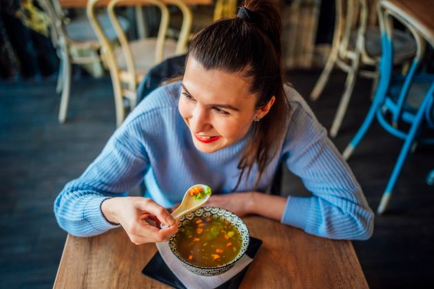 Young cheerful woman eating vegetable soup at restaurant